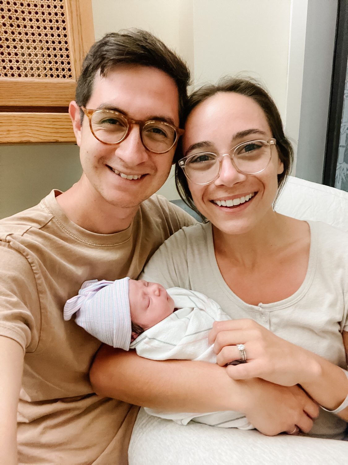 Smiling couple holding a newborn baby in a cozy bedroom