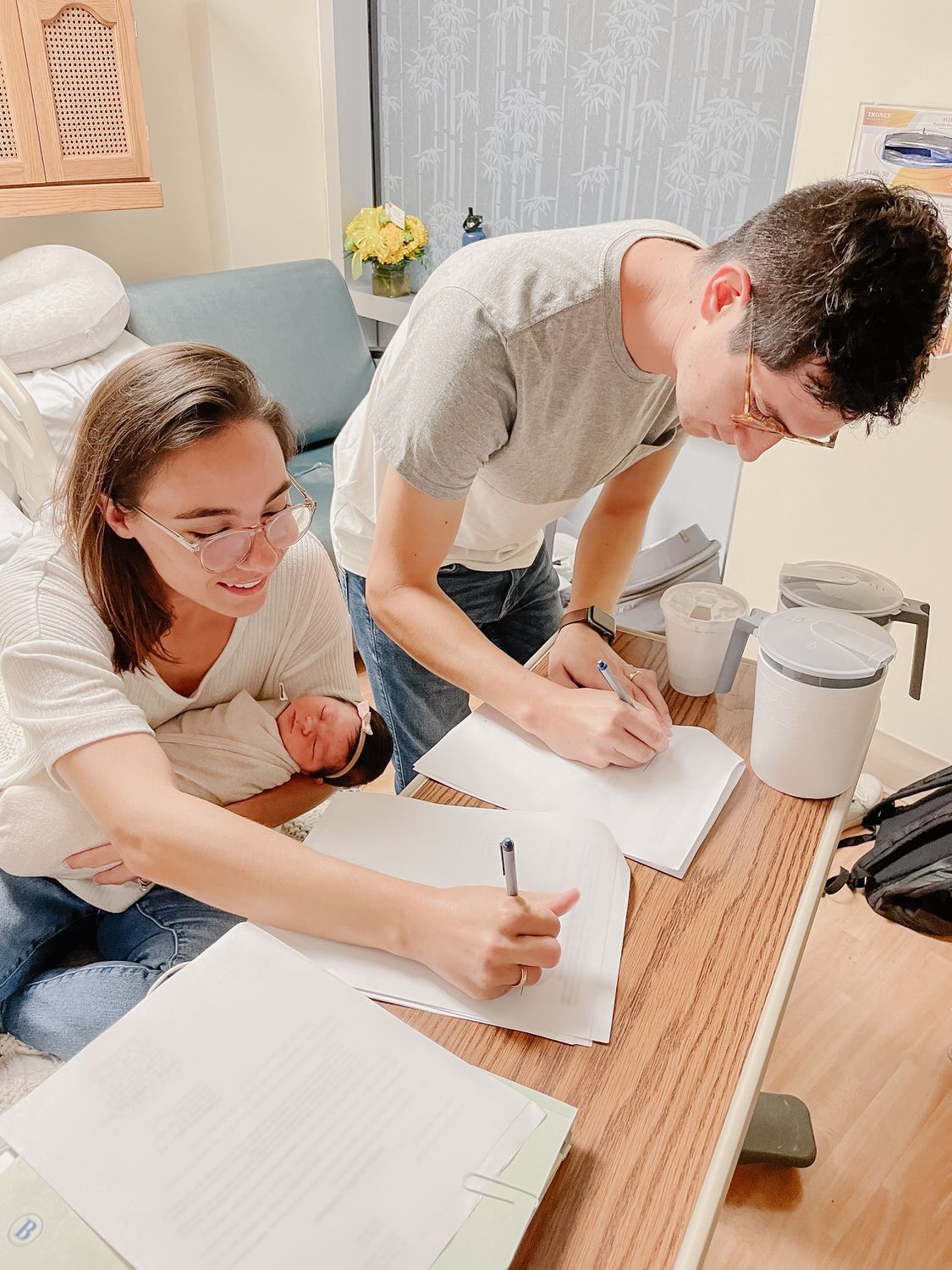 Two people writing on papers at a table in a bright room