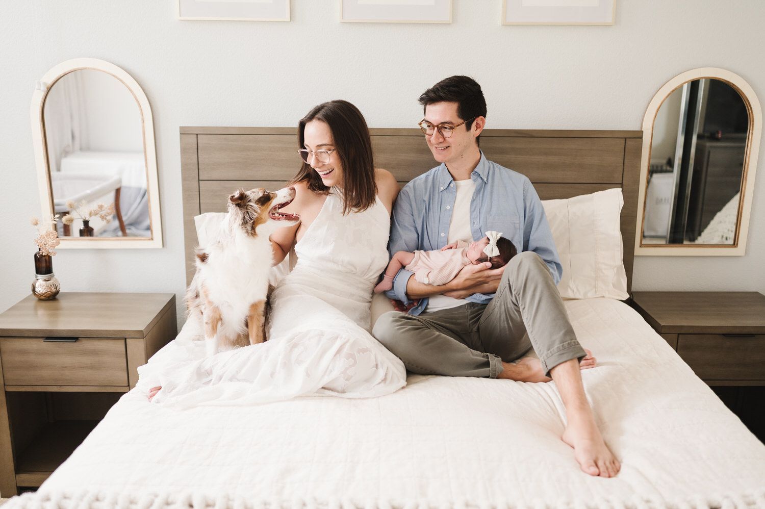 Couple sitting on a bed with their dog and baby in a bright bedroom