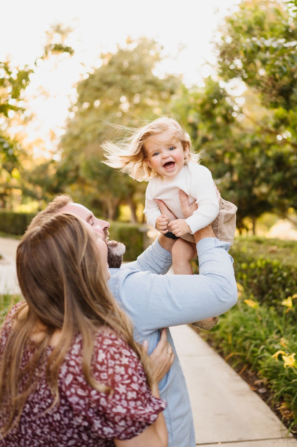 A man and woman are holding a baby in their arms in a park.