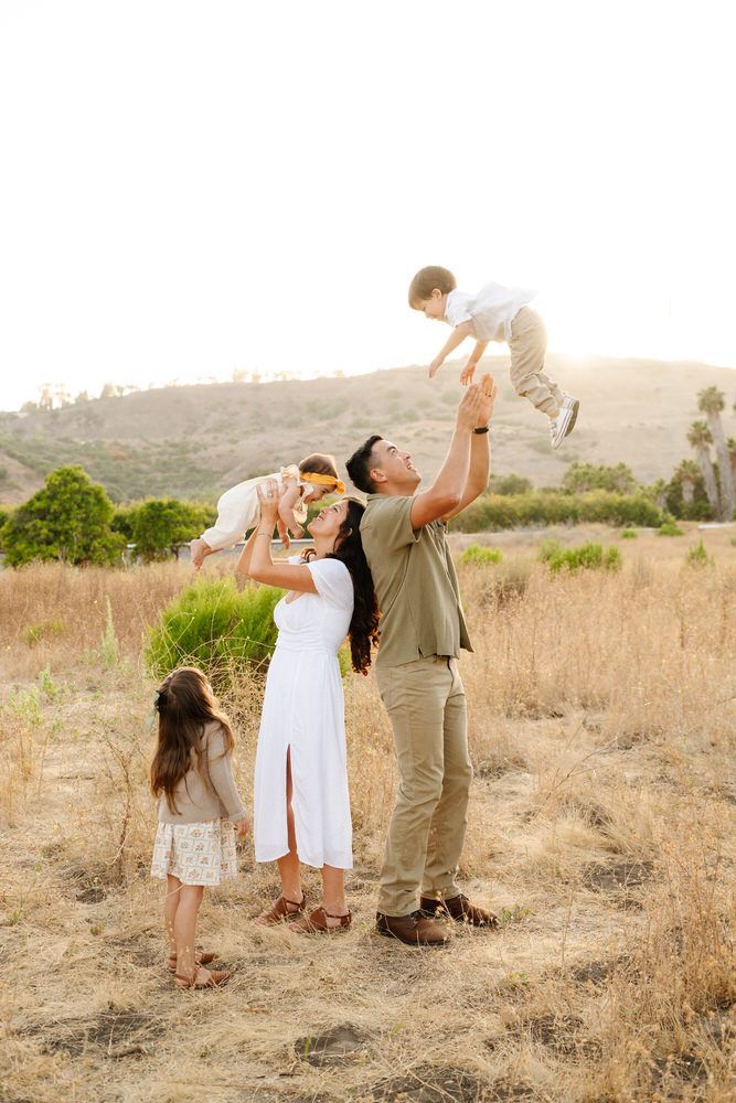 Family standing in a dry field, lifting a child into the air at sunset