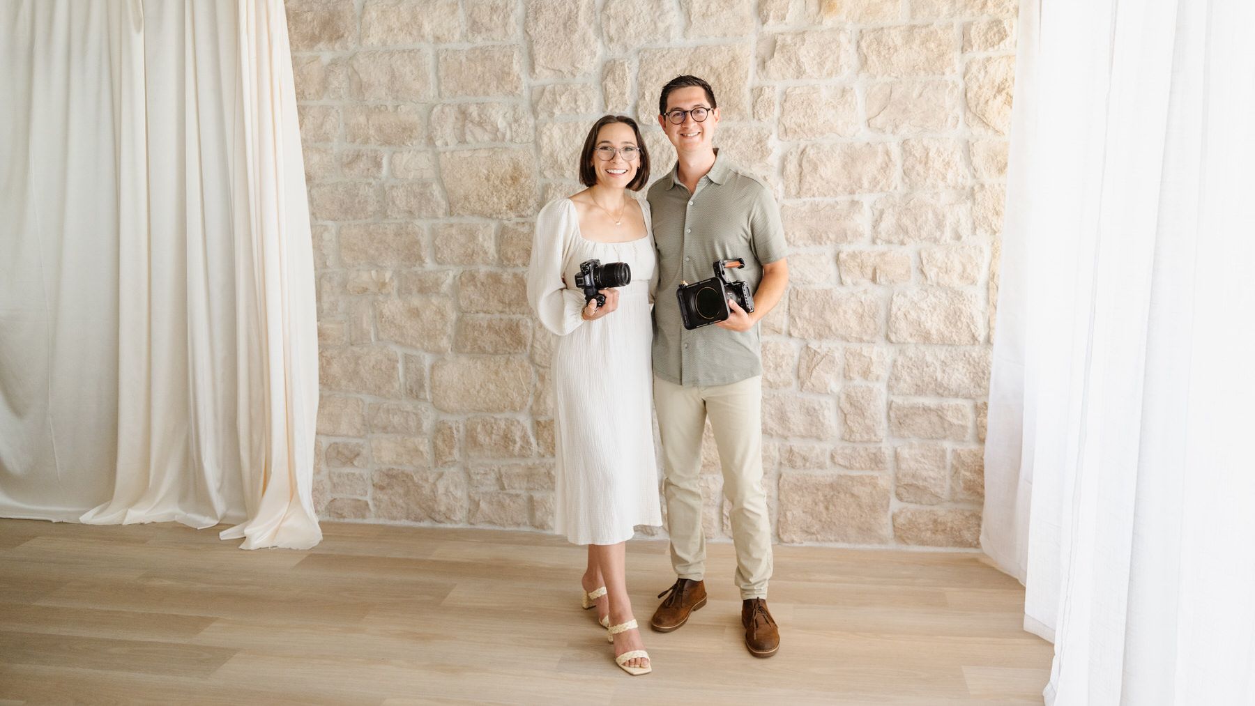 Dan and Tyler holding cameras in front of a stone wall