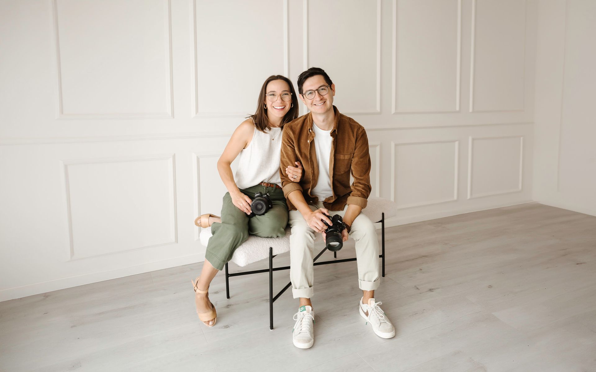 Two people sitting on chairs in a bright white room, smiling at the camera at Huntington Beach studio
