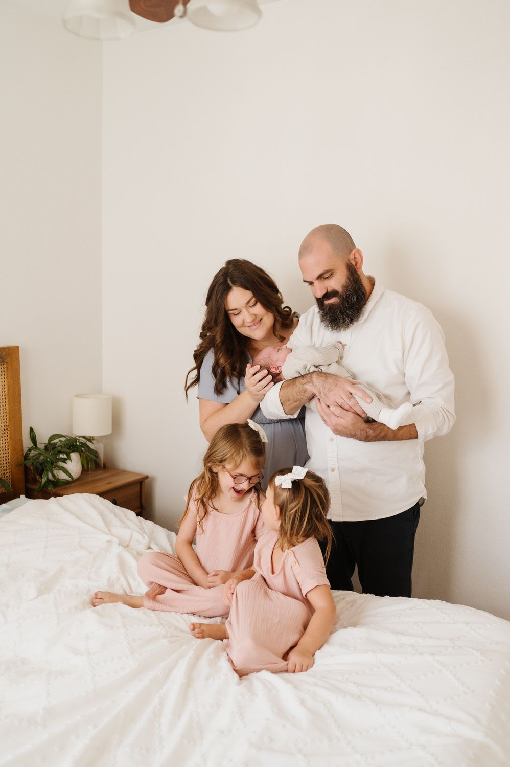 A family is sitting on a bed holding a newborn baby.