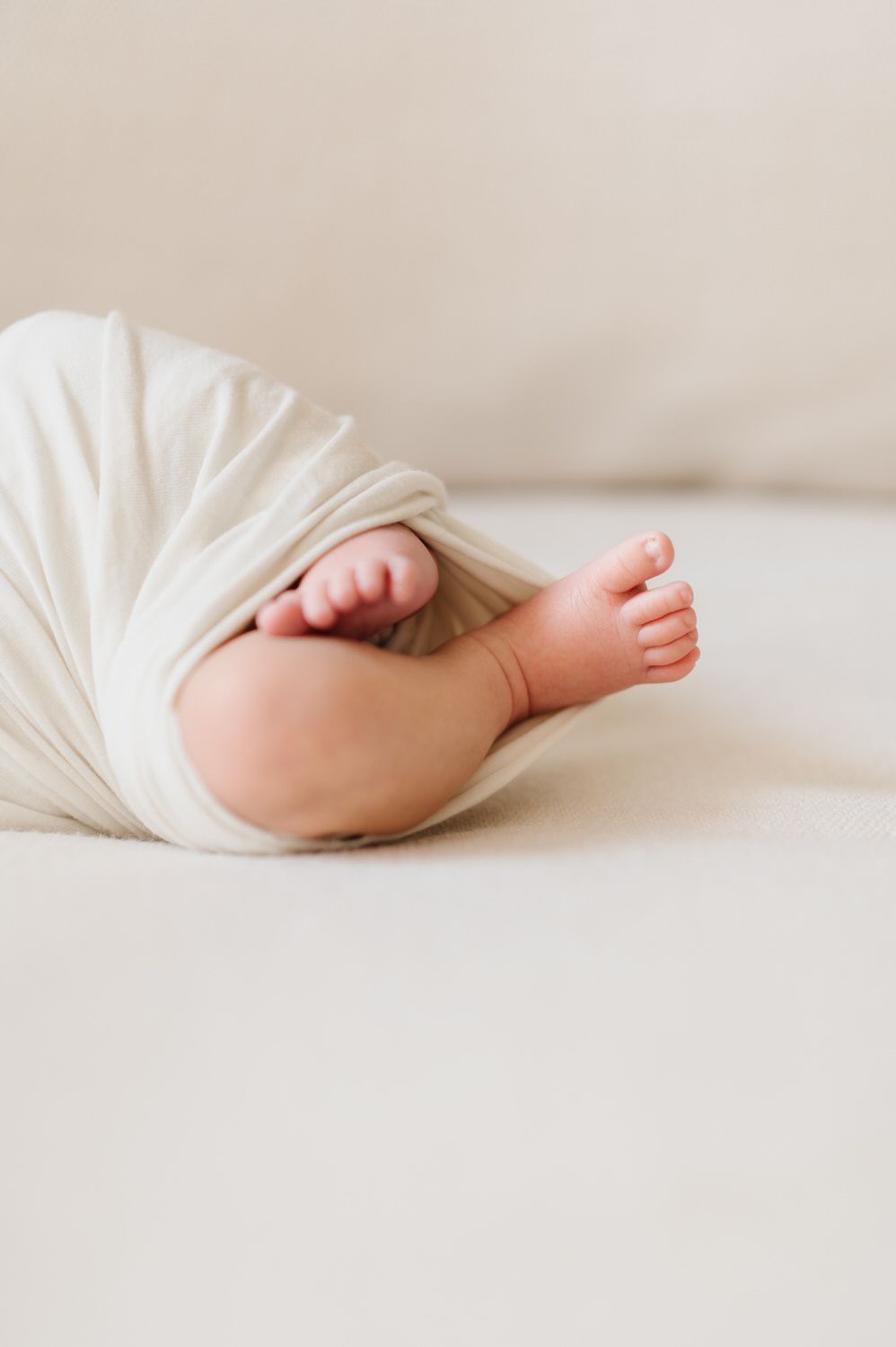 A newborn baby wrapped in a white blanket is laying on a bed for an in home newborn photo in Orange County.