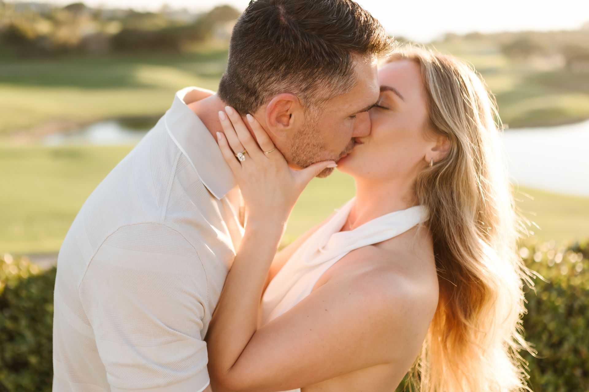 Couple kissing outdoors in warm sunlight, with a blurred grassy background for a proposal with The Yes Girls