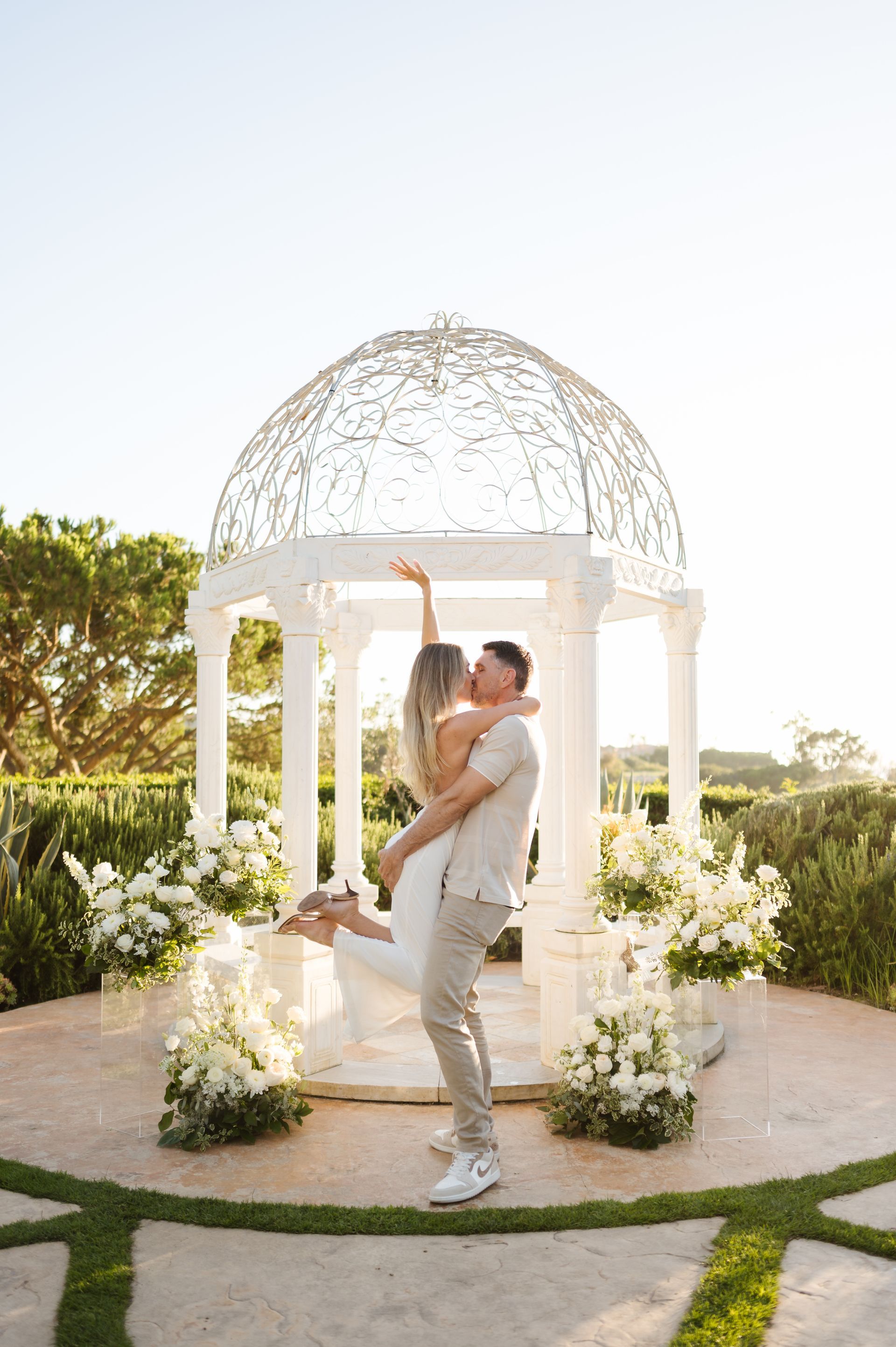 Couple embracing in a white gazebo garden proposal setting with The Yes Girls with flowers and sunlight