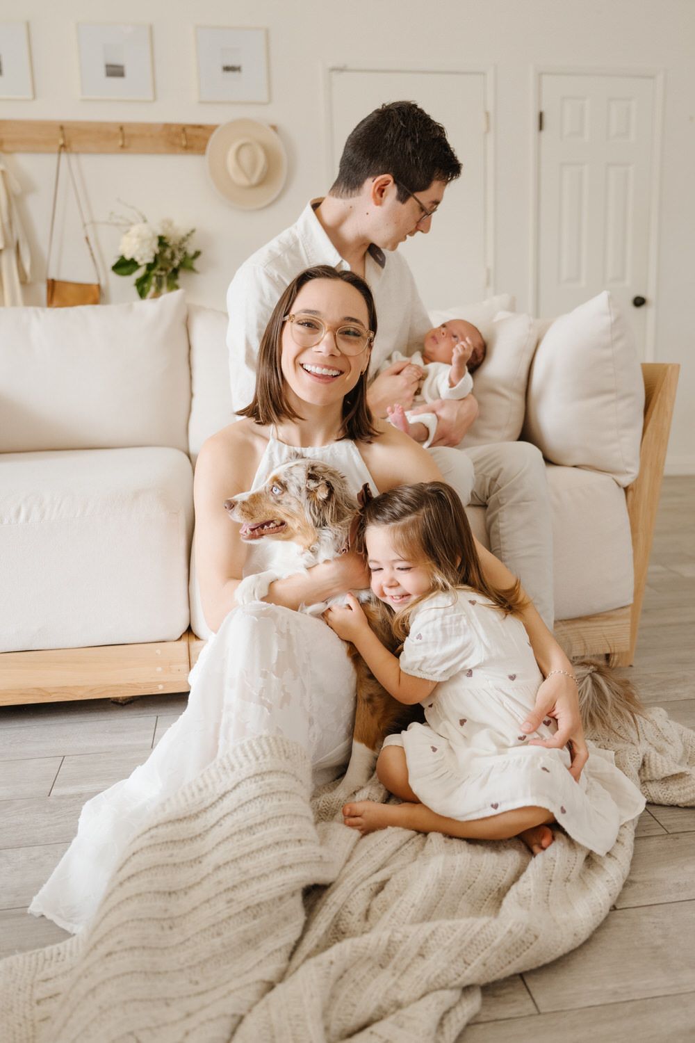 Family posing in a cozy living room with a dog, a baby, and two children on a cream sofa and rug