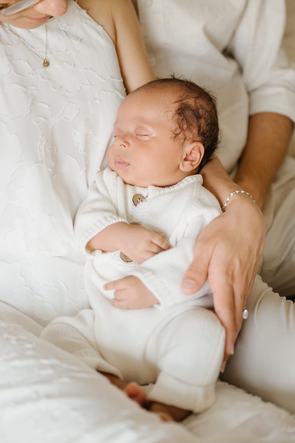Sleeping baby in white clothes cradled in an adult’s arms on a couch