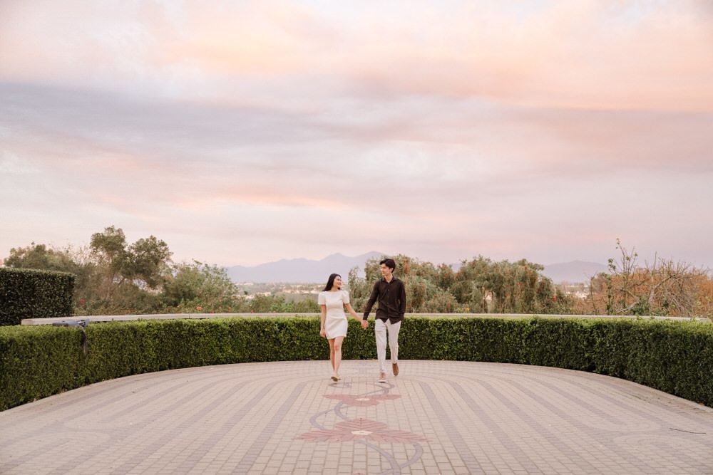 Two people walking on a circular terrace with hedges at sunset
