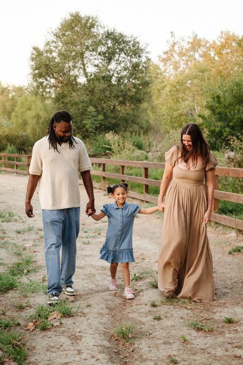 Three people walking hand in hand on a dirt path by a wooden fence and trees in Laguna Hills.