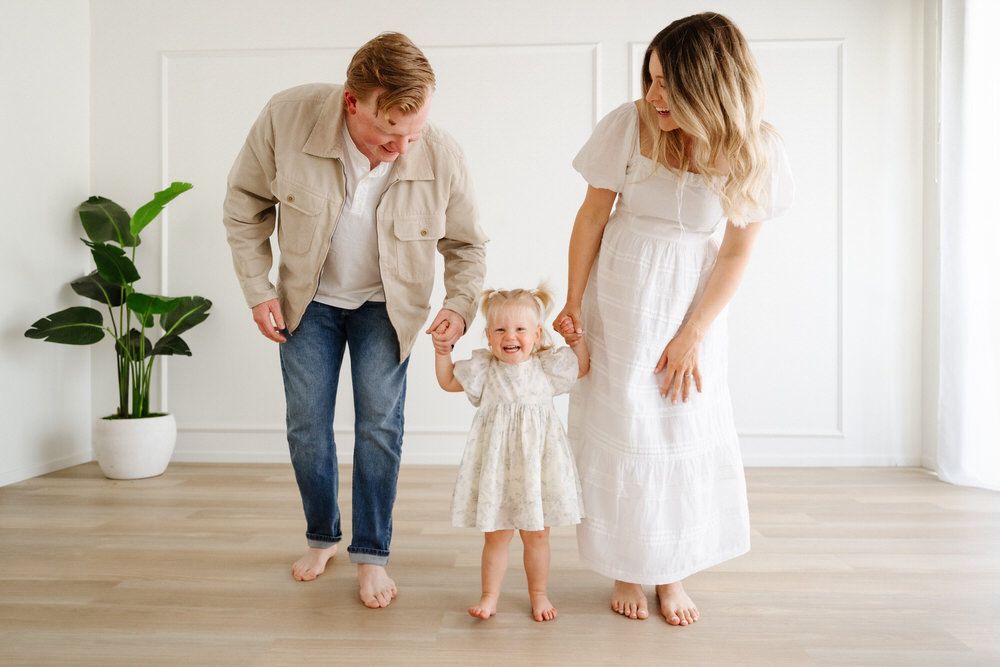 Family of three holding hands and walking barefoot in a bright, minimalist room