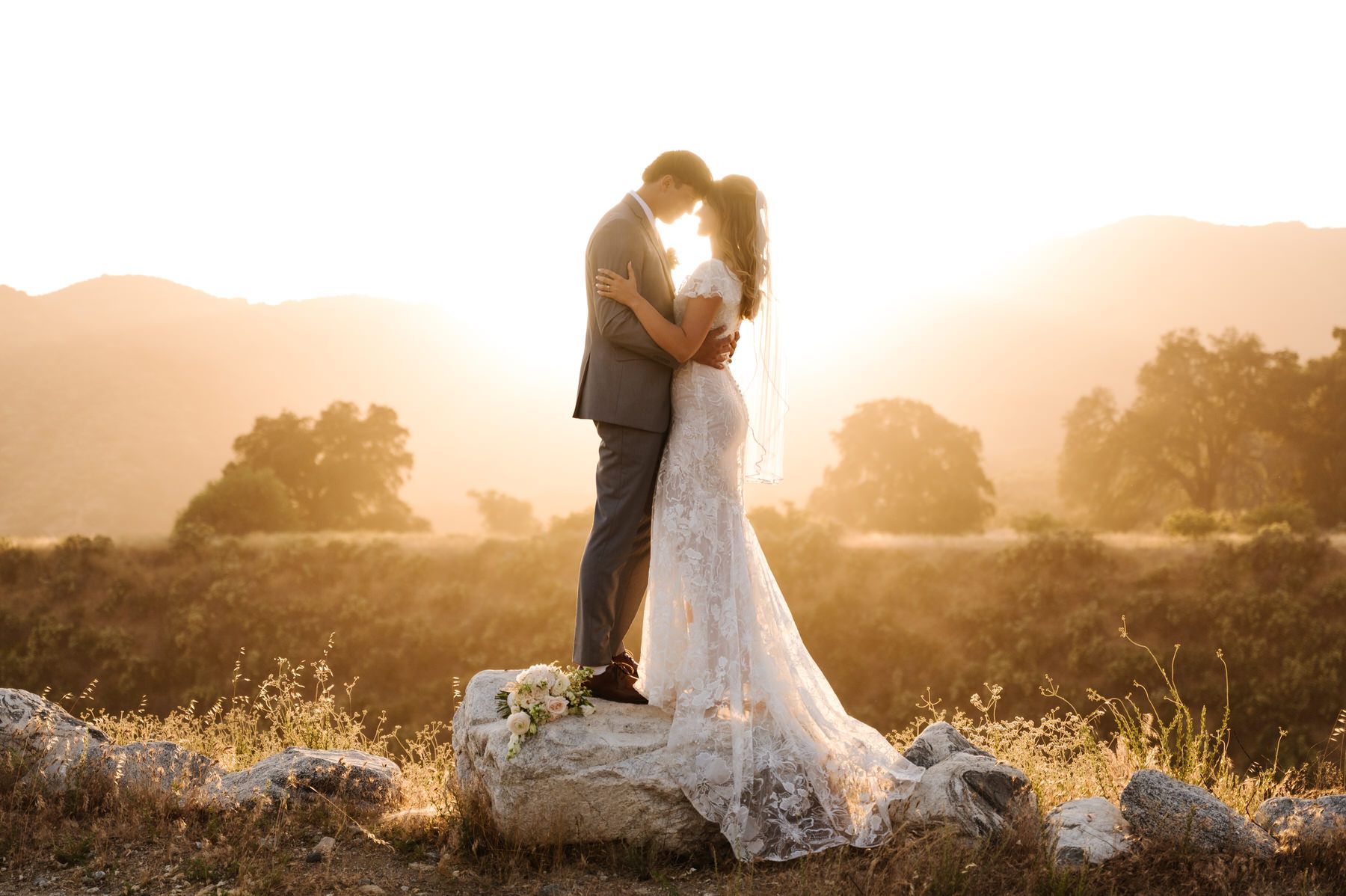 Couple embracing on a rock at sunset in a warm golden field