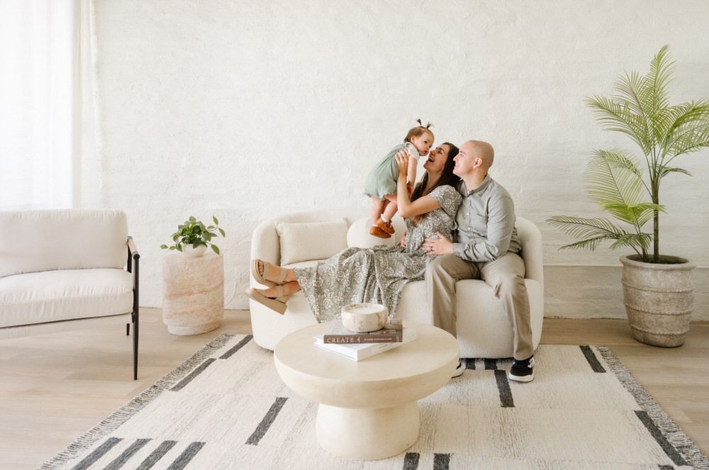 Two people sitting on a white couch in a bright living room with a small dog and potted plants