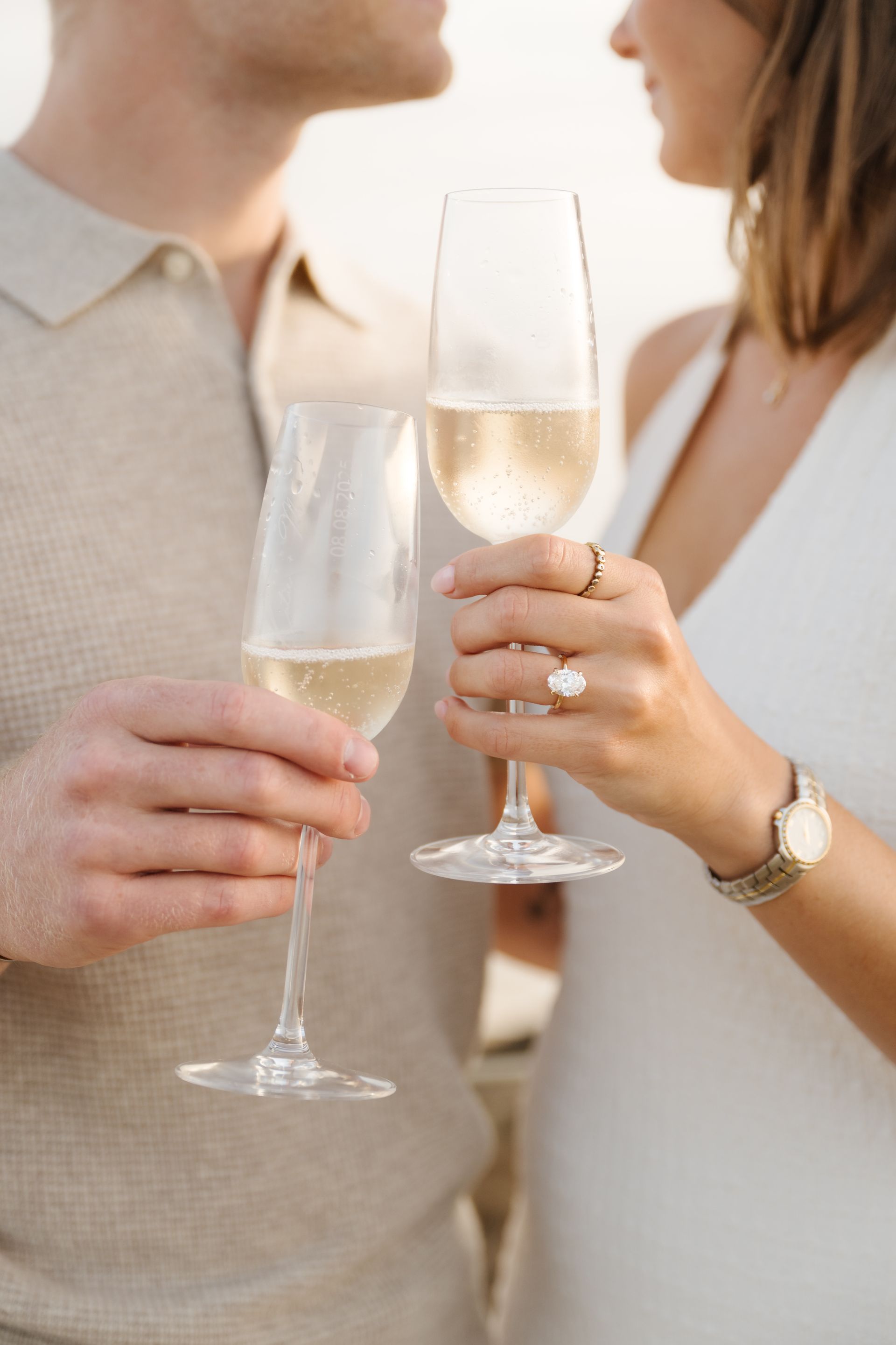 Two people clink champagne flutes, wearing neutral-toned clothing for a proposal with The Yes Girls