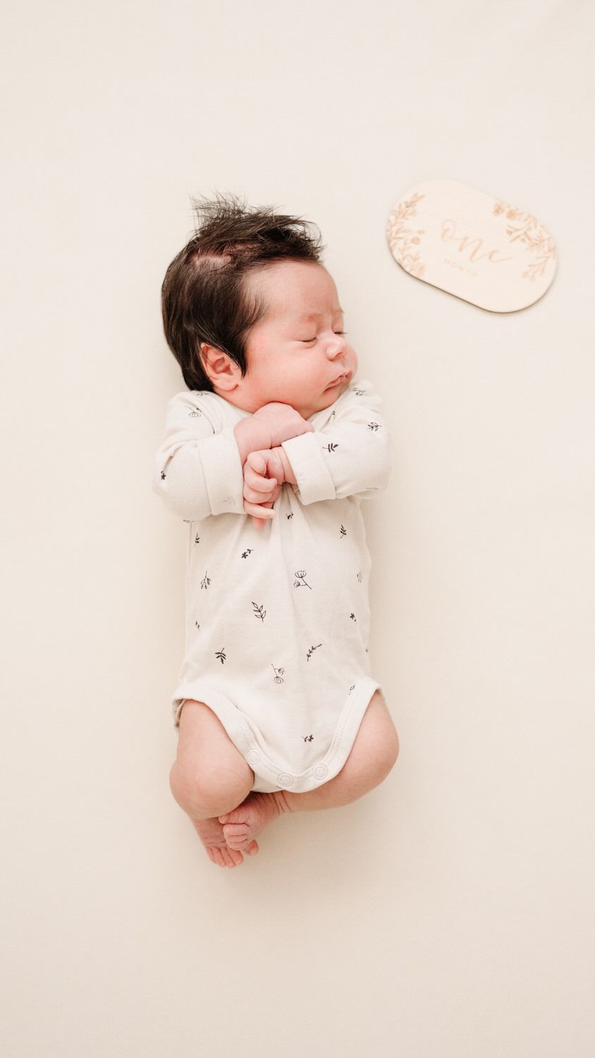 Newborn baby sleeping on a cream blanket beside a small cloud-shaped pillow
