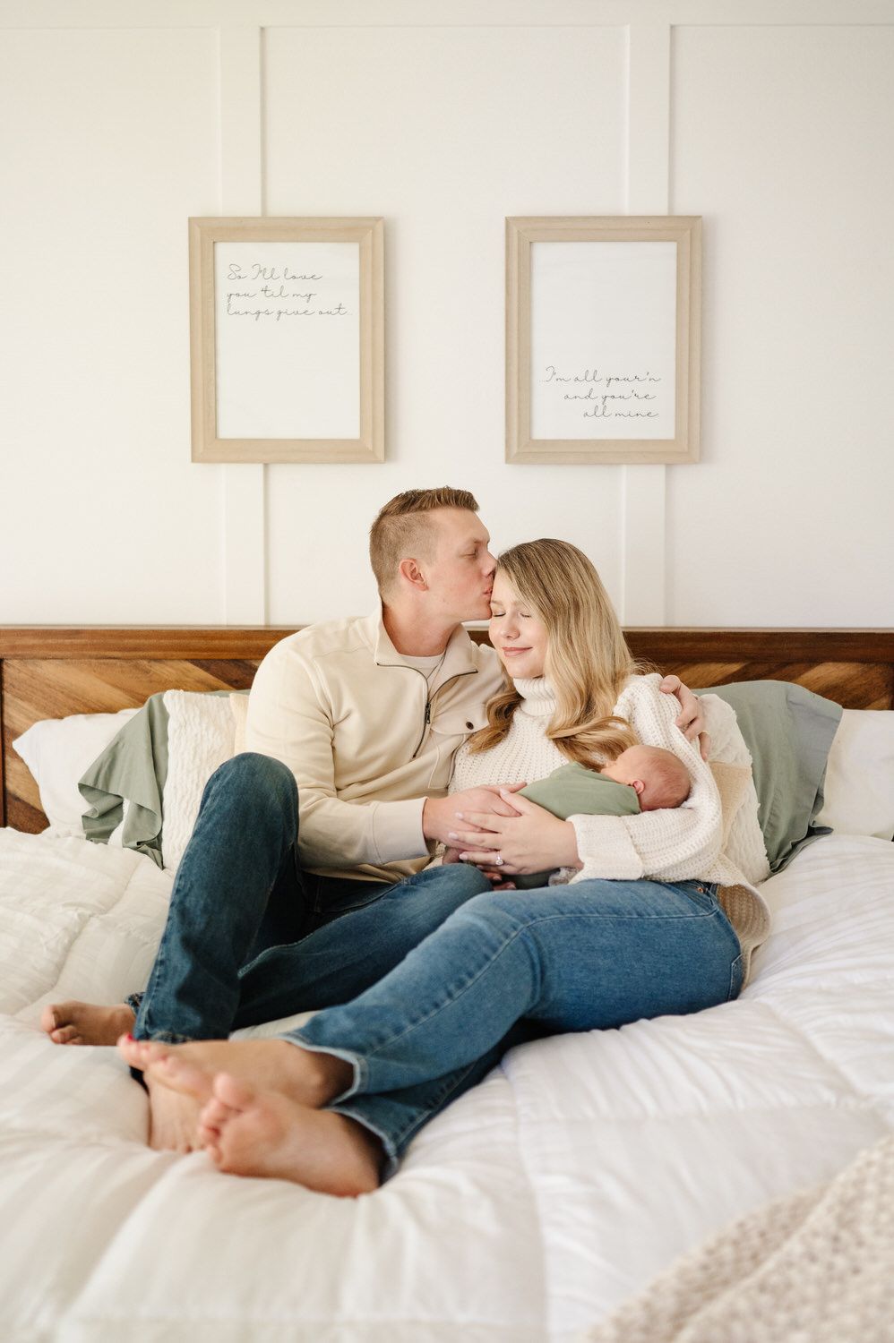 A man and woman are sitting on a bed with a newborn baby.