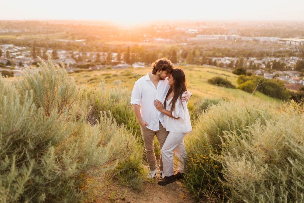 Couple in white clothes walking through tall grass at sunset in a golden field