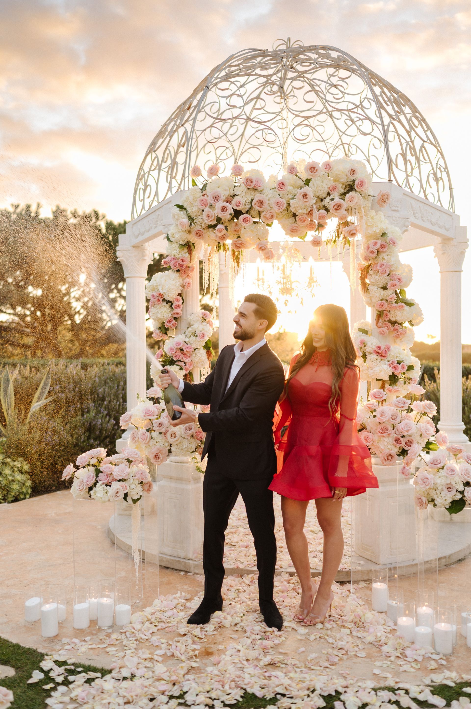 Couple standing by a flower-covered wedding gazebo at sunset for a proposal with The Yes Girls