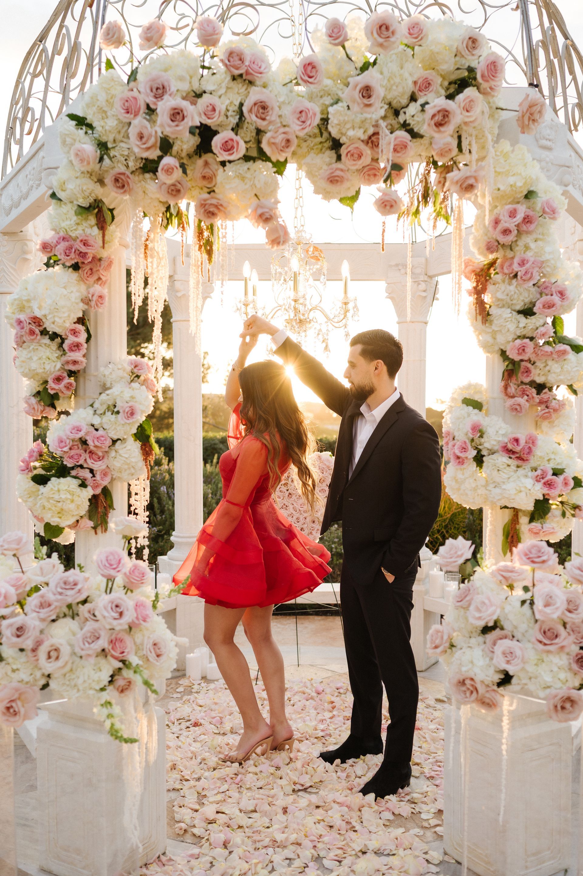 Couple standing under a floral arch for a proposal with The Yes Girls, with pink and white flowers and soft lights