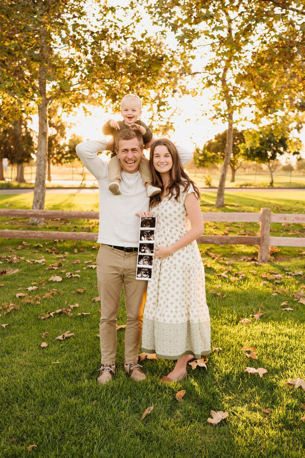 A man and woman are standing in the grass with a baby on their shoulders.