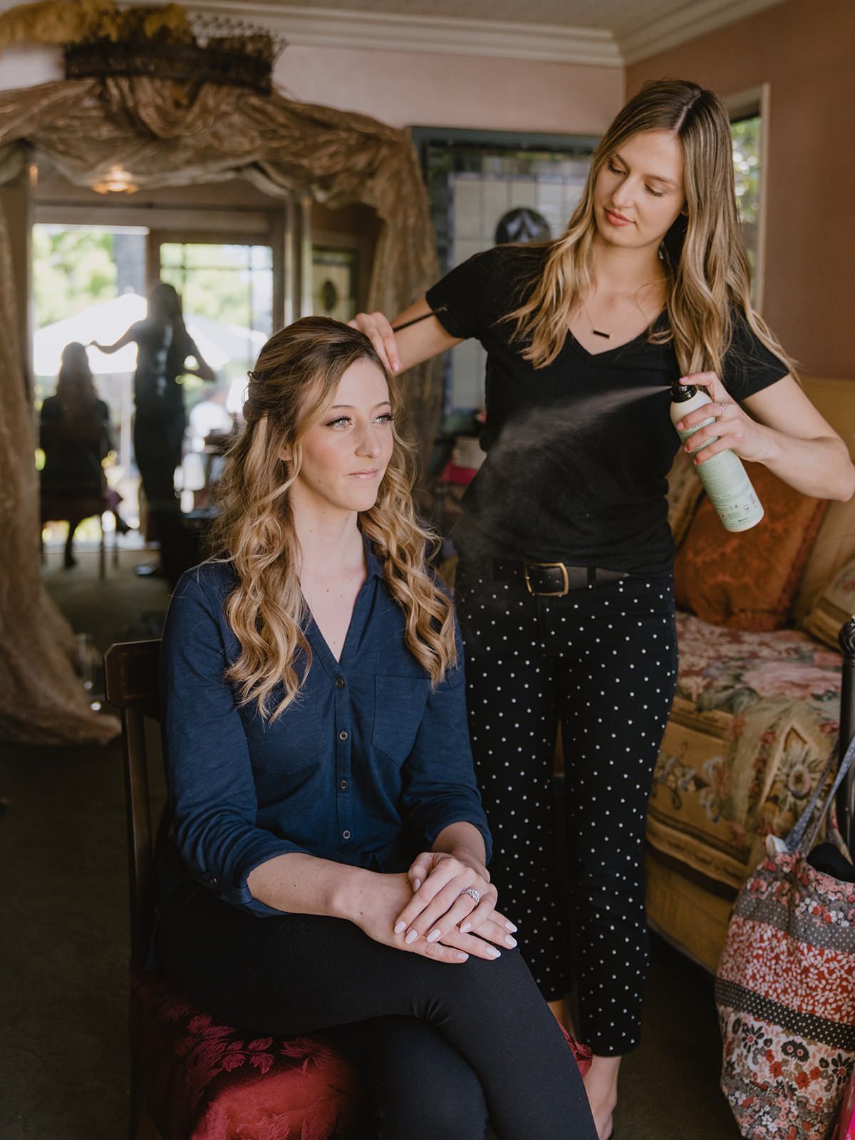 A stylist uses hairspray on a bride with wavy hair.