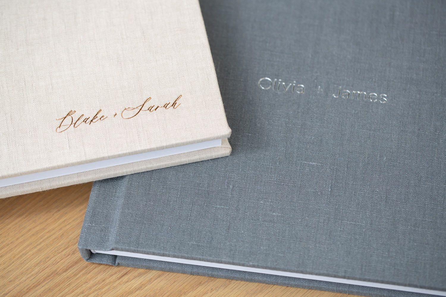 Two personalized hardcover wedding albums, cream and gray, on a wooden surface.