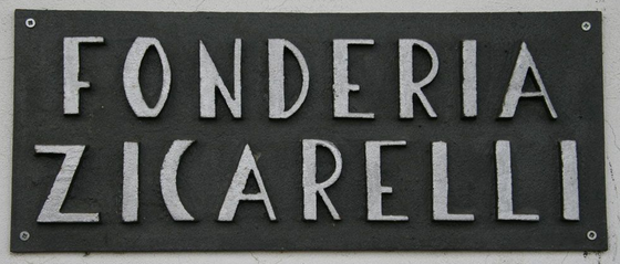 Insegna nera con la scritta “FONDERIA ZICARELLI” fissata a una parete bianca.
