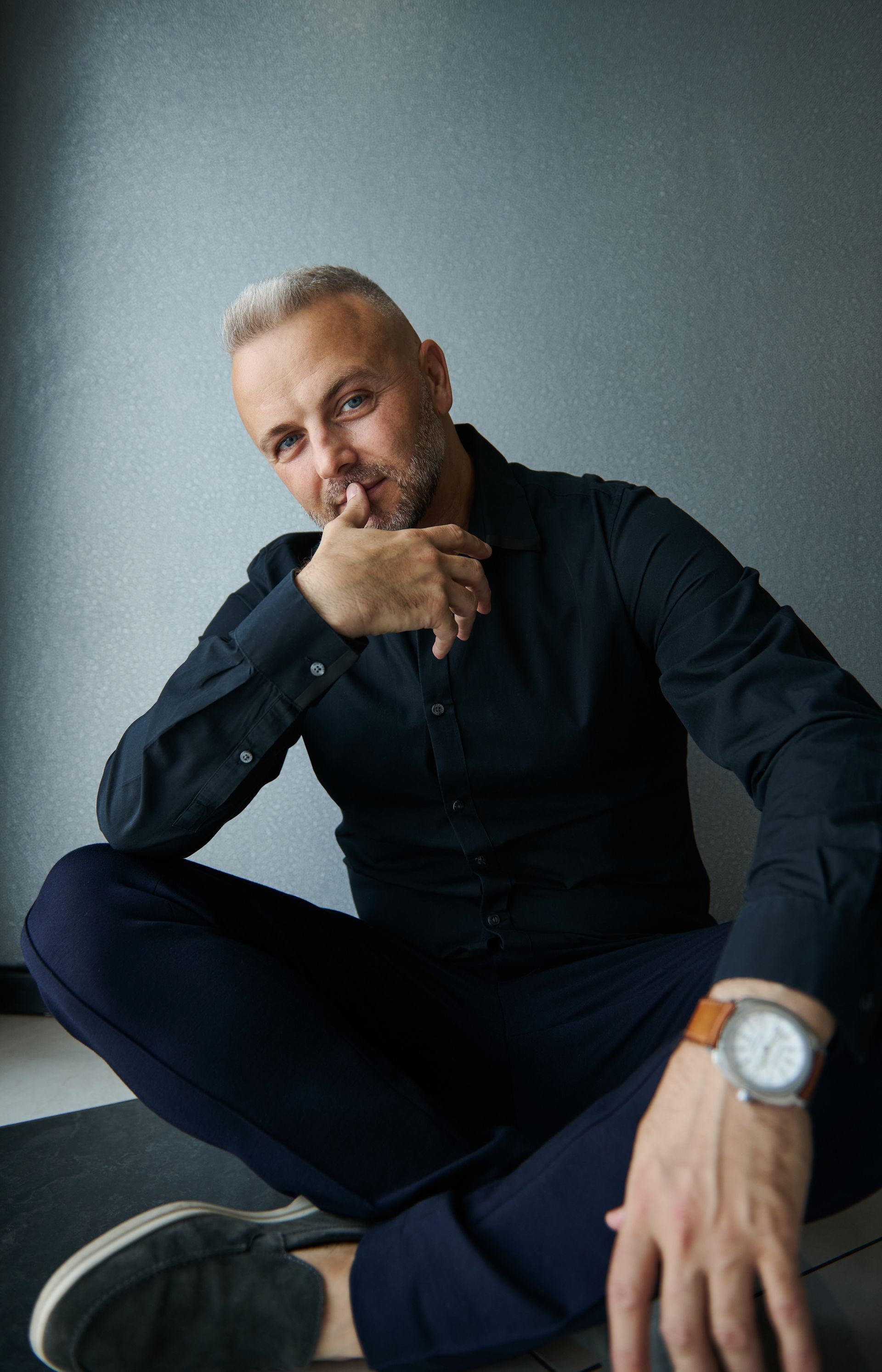 A man is sitting on the floor wearing a watch and a black shirt.