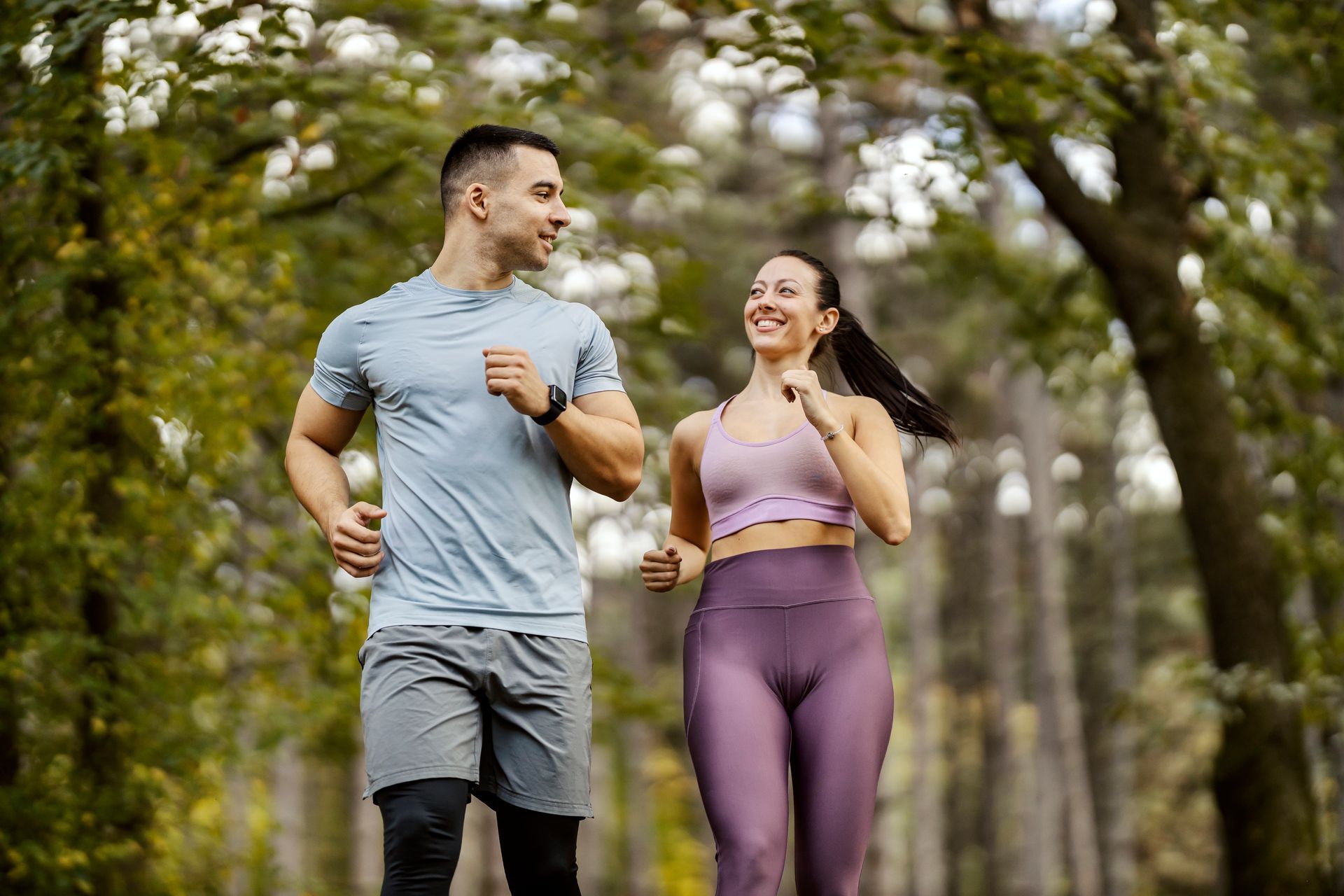 A man and a woman are jogging in the woods.