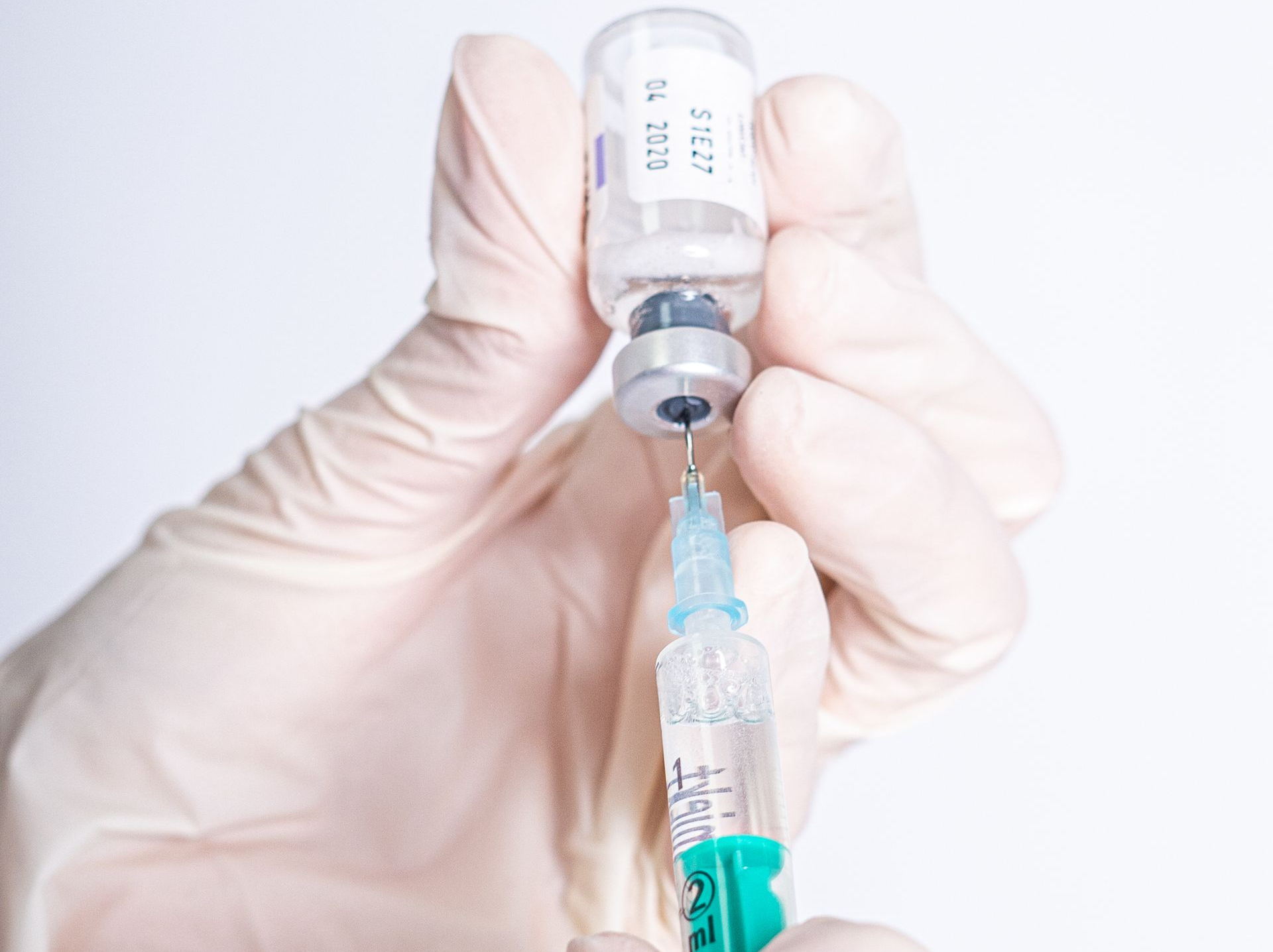 Gloved hand drawing liquid from a vial into a syringe