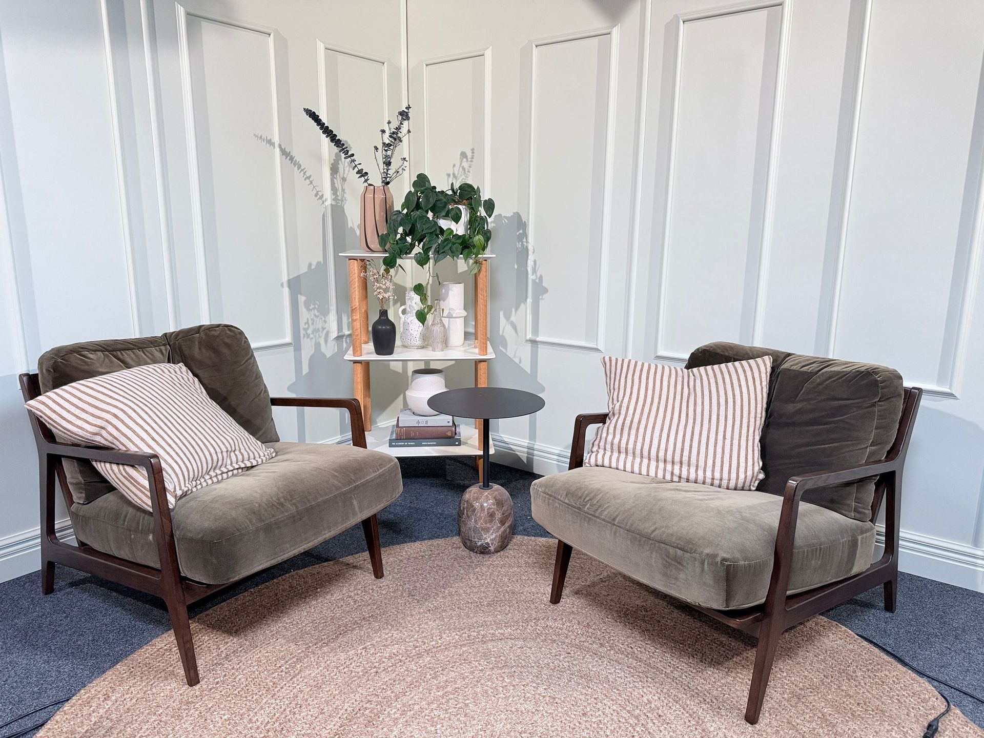 Two beige armchairs in a bright corner with a small round table and decorative plants.