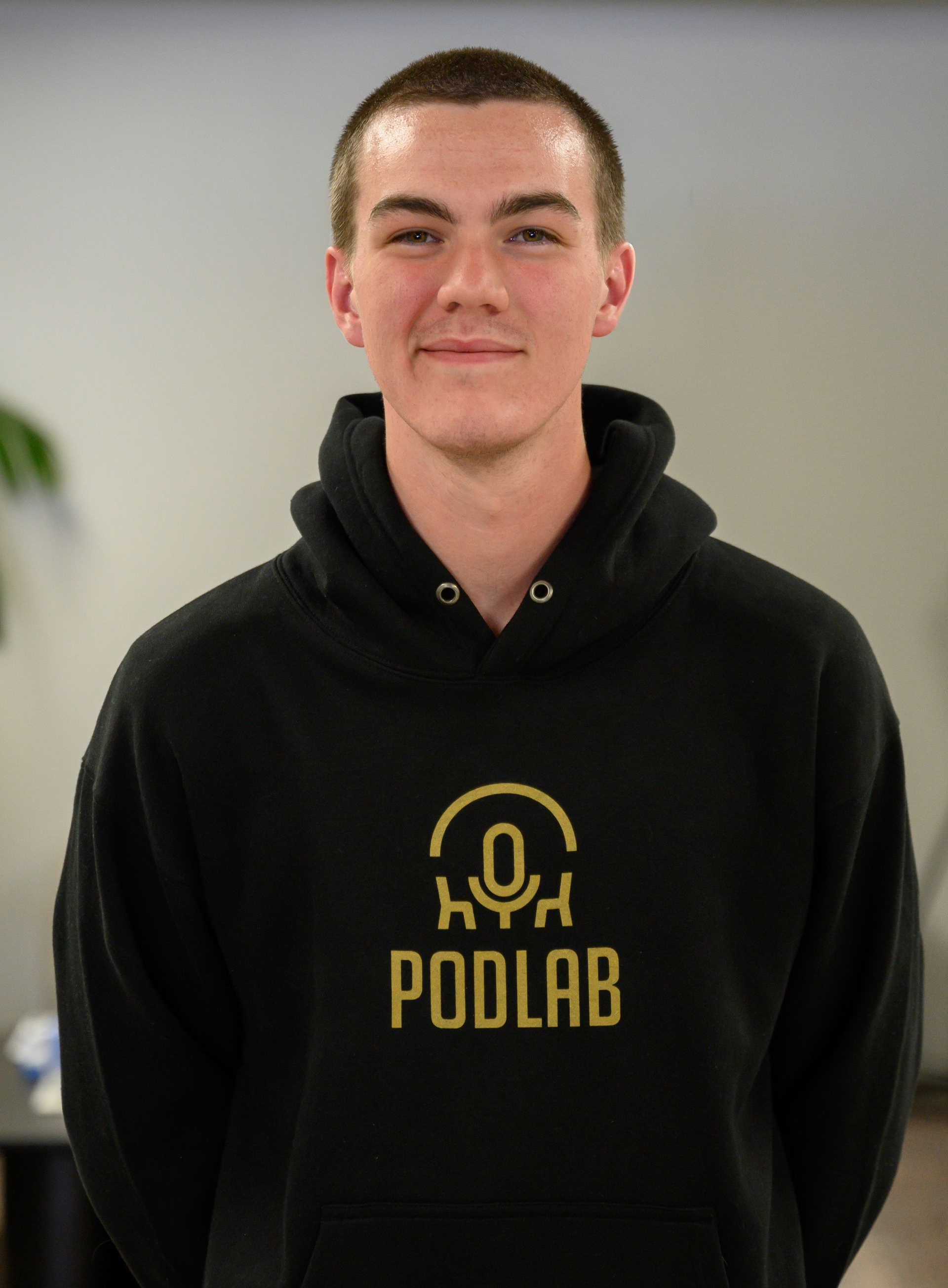 Young person in a black PODLAB hoodie, standing and smiling indoors.
