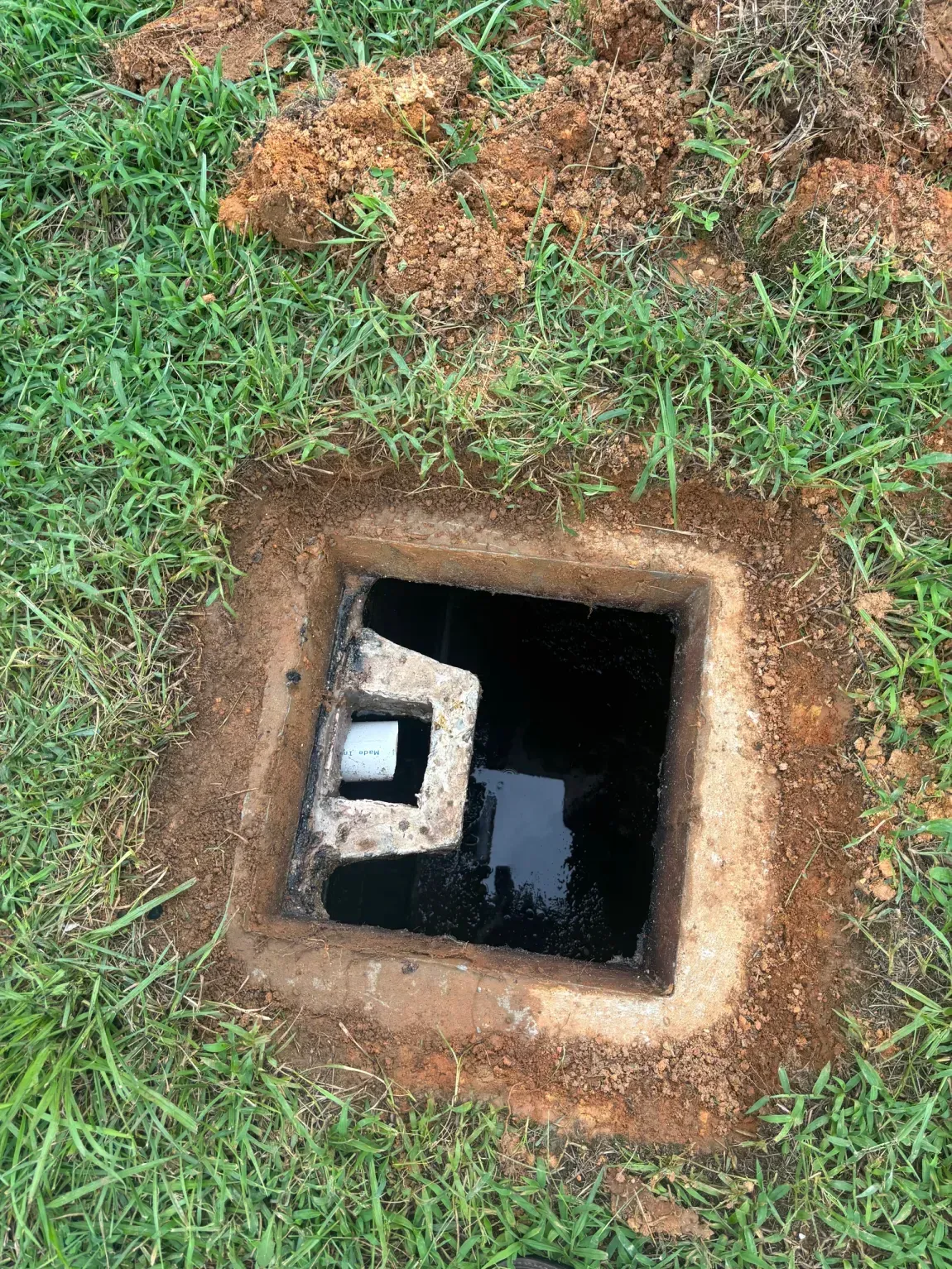 Open square utility access hole in grass with dark water inside