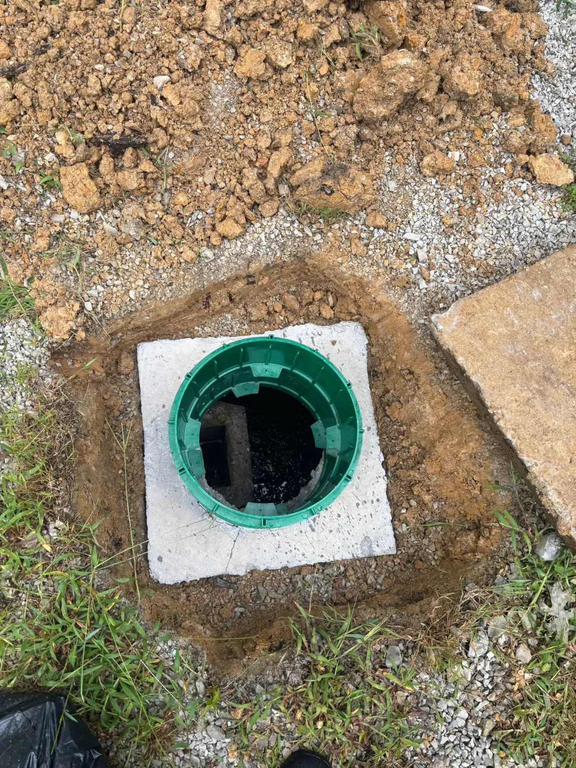 Green utility access pipe set in a concrete square on the ground near soil and grass