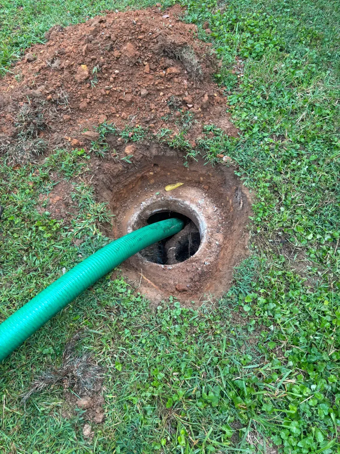 Green hose entering a circular hole in the ground beside a small dirt mound on grass
