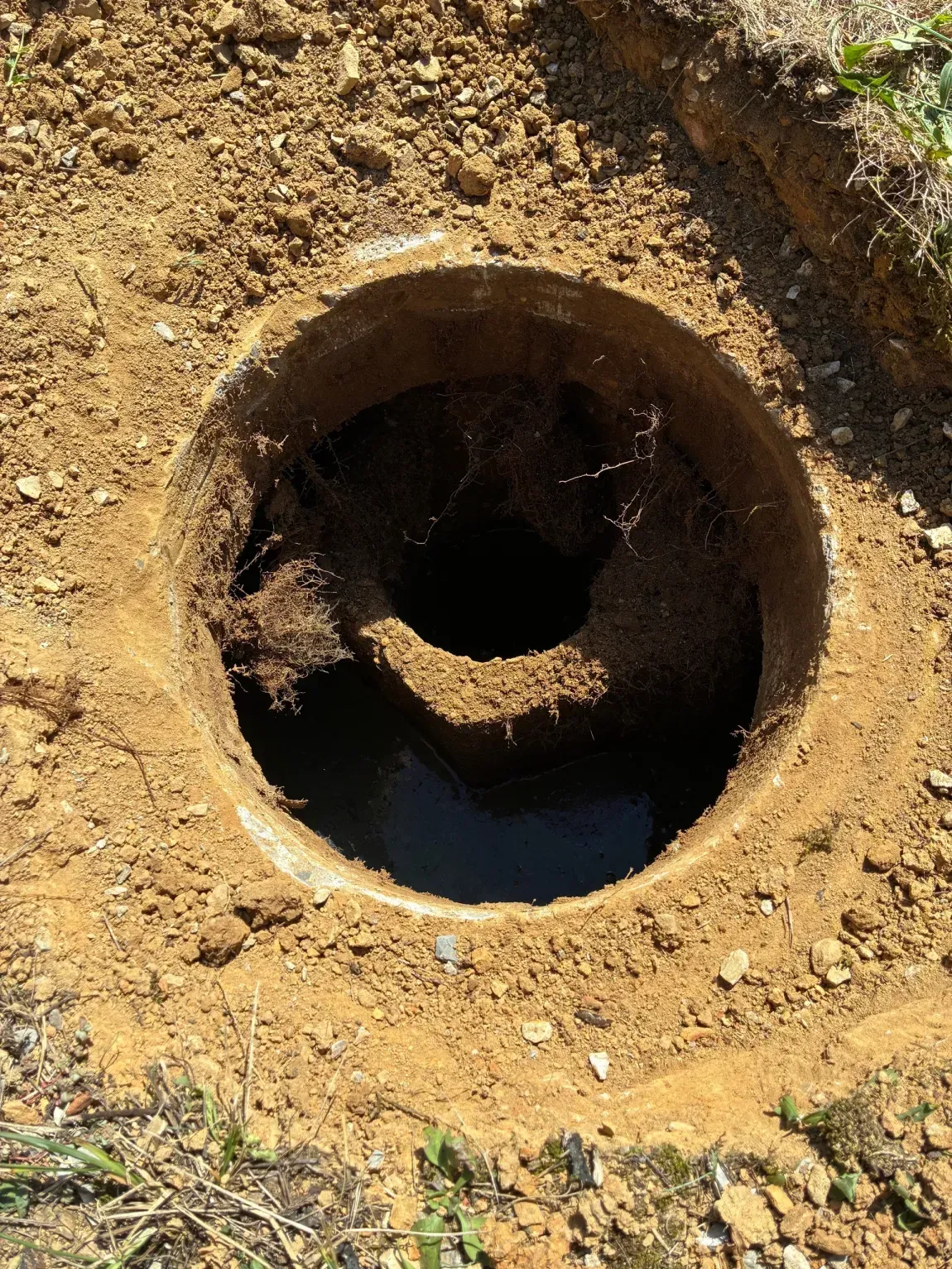Rusty circular metal pipe opening in dry dirt, with a dark tunnel inside.