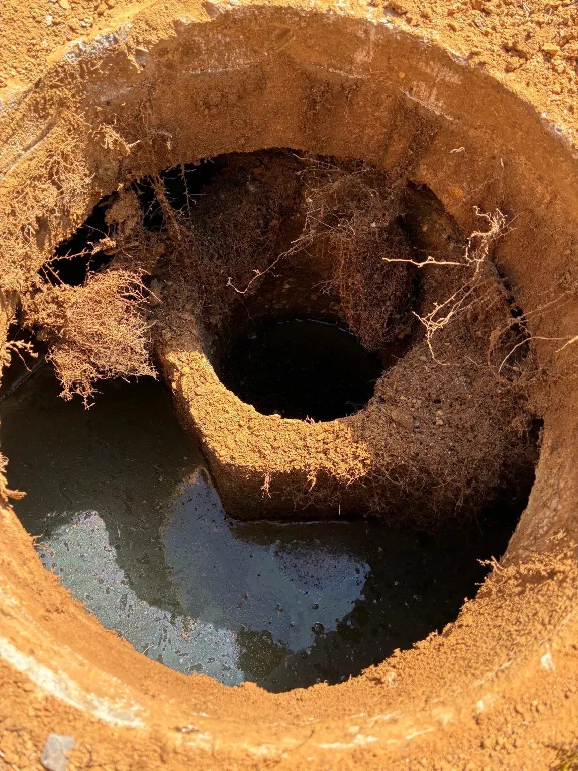 Rust-colored spiral excavation pit with dark water at the bottom, viewed from above.