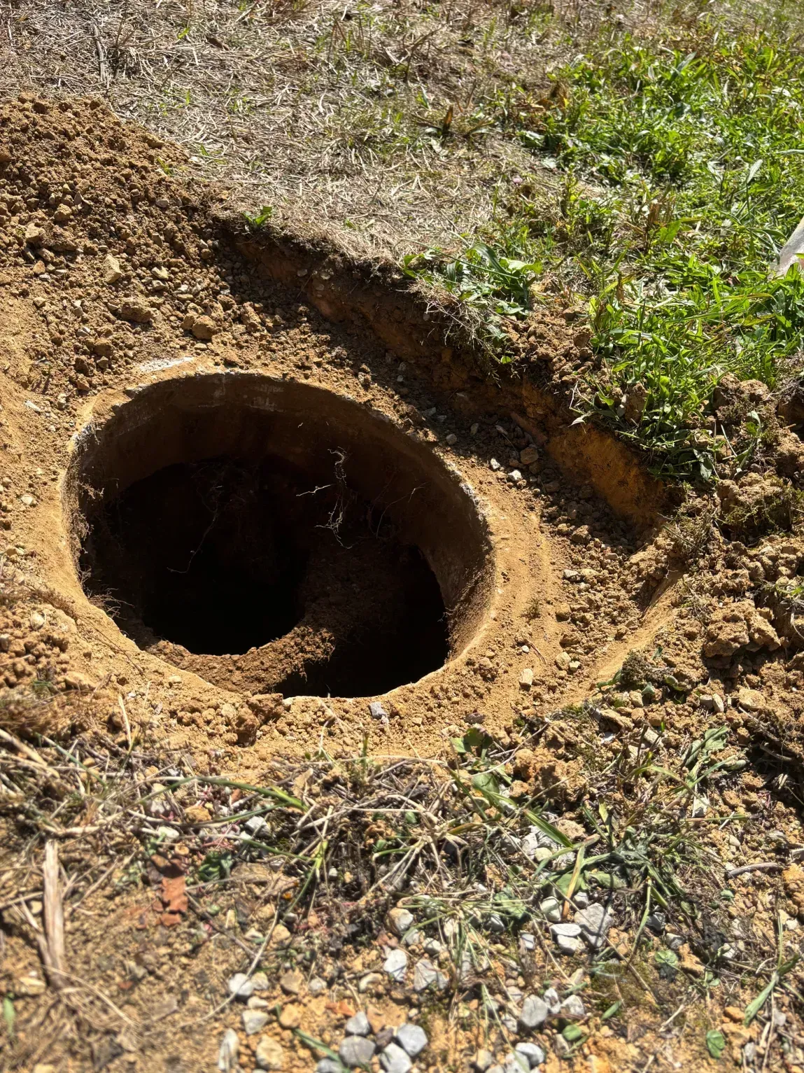A large round hole in the ground with exposed dirt and grass around it.