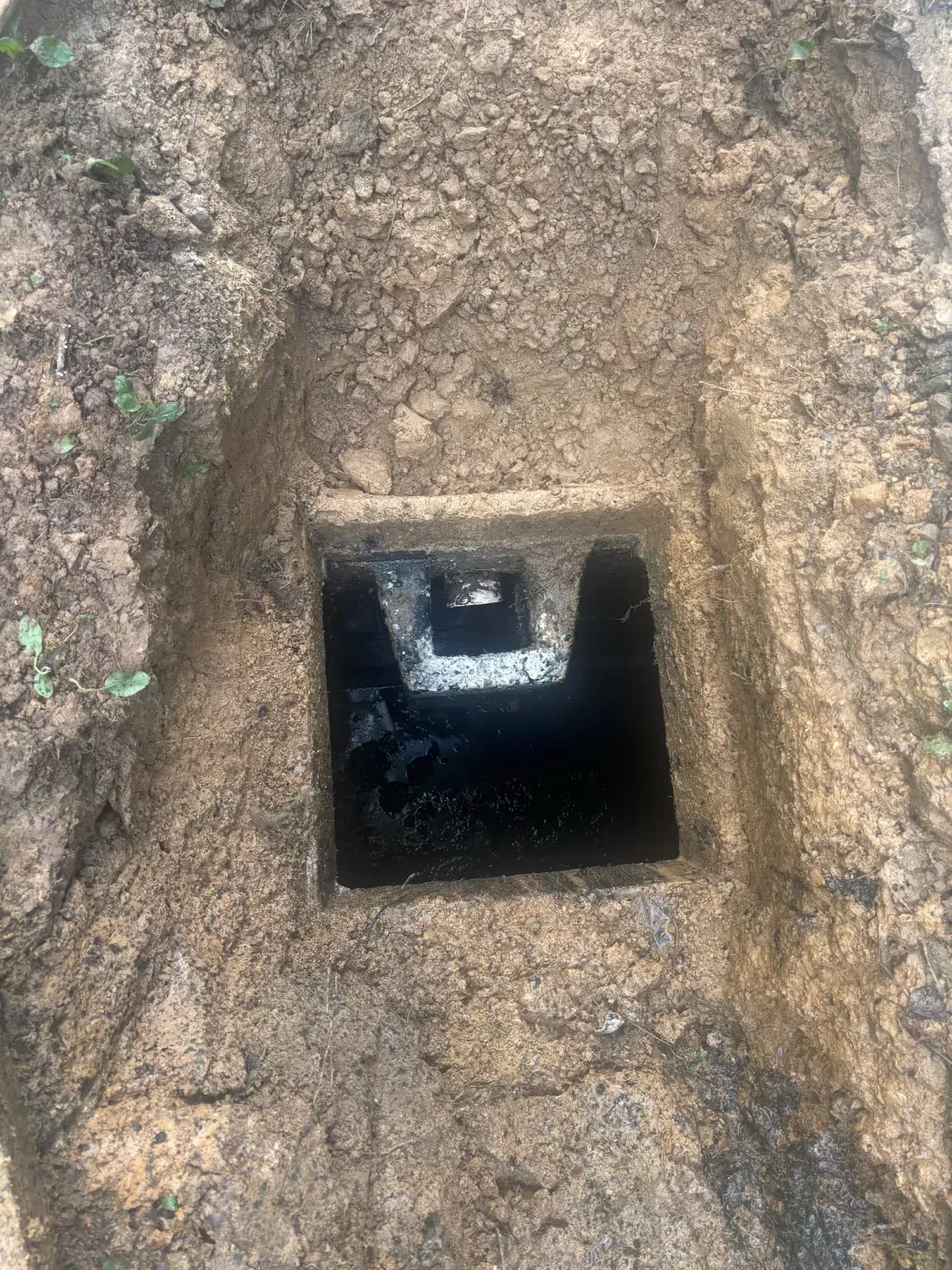 Square hole in muddy ground showing a dark underground shaft.