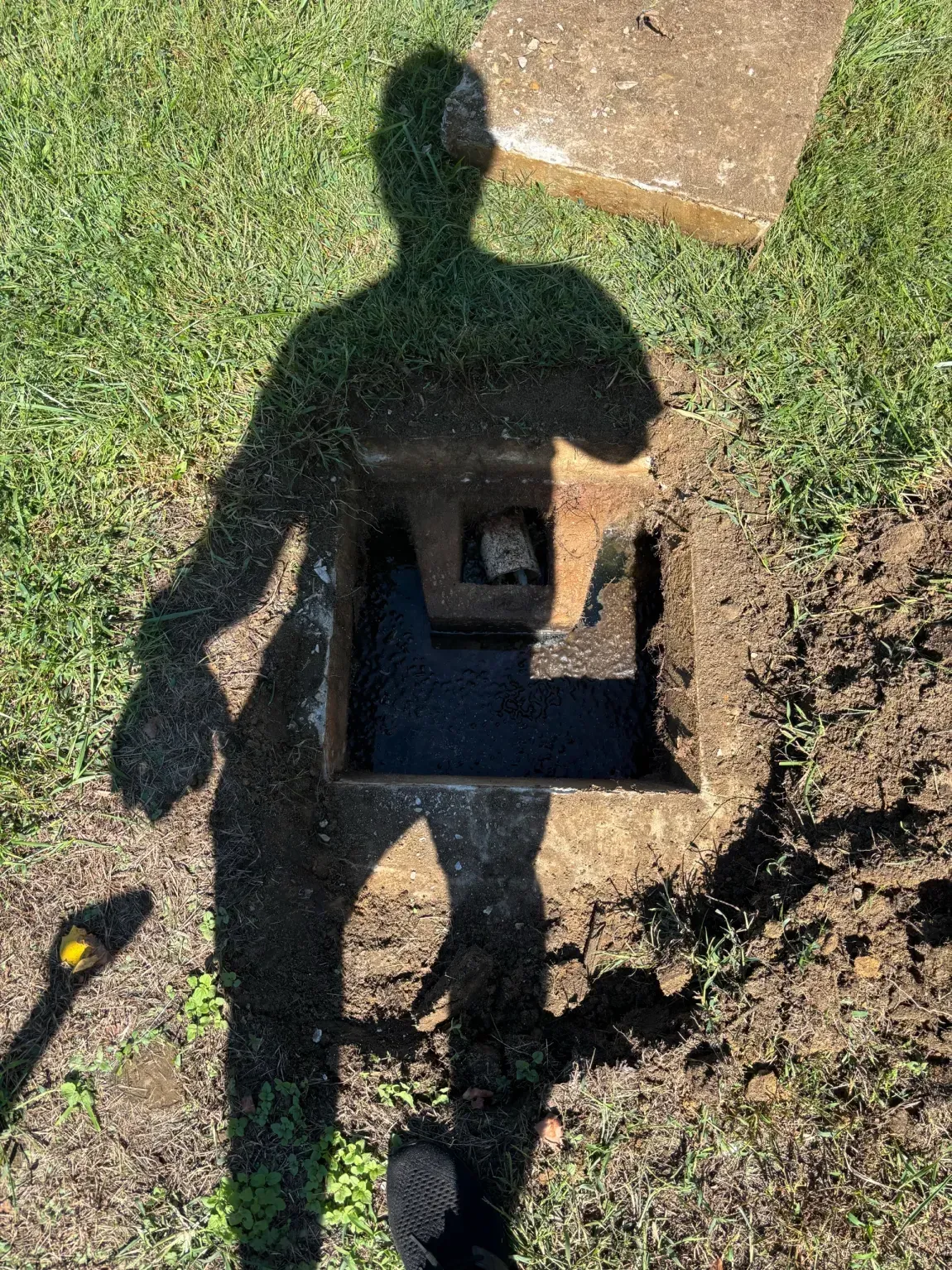 Shadow of a person over an open utility meter box in a grassy yard