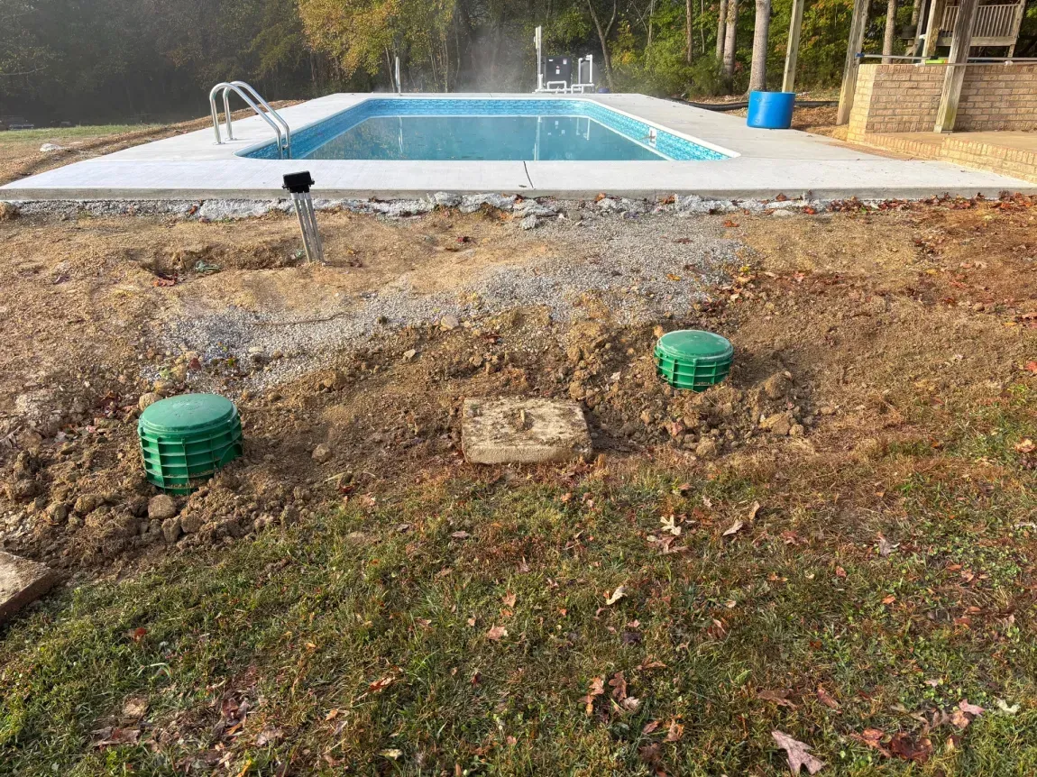 Backyard pool with rocky landscaping and green utility covers in the foreground