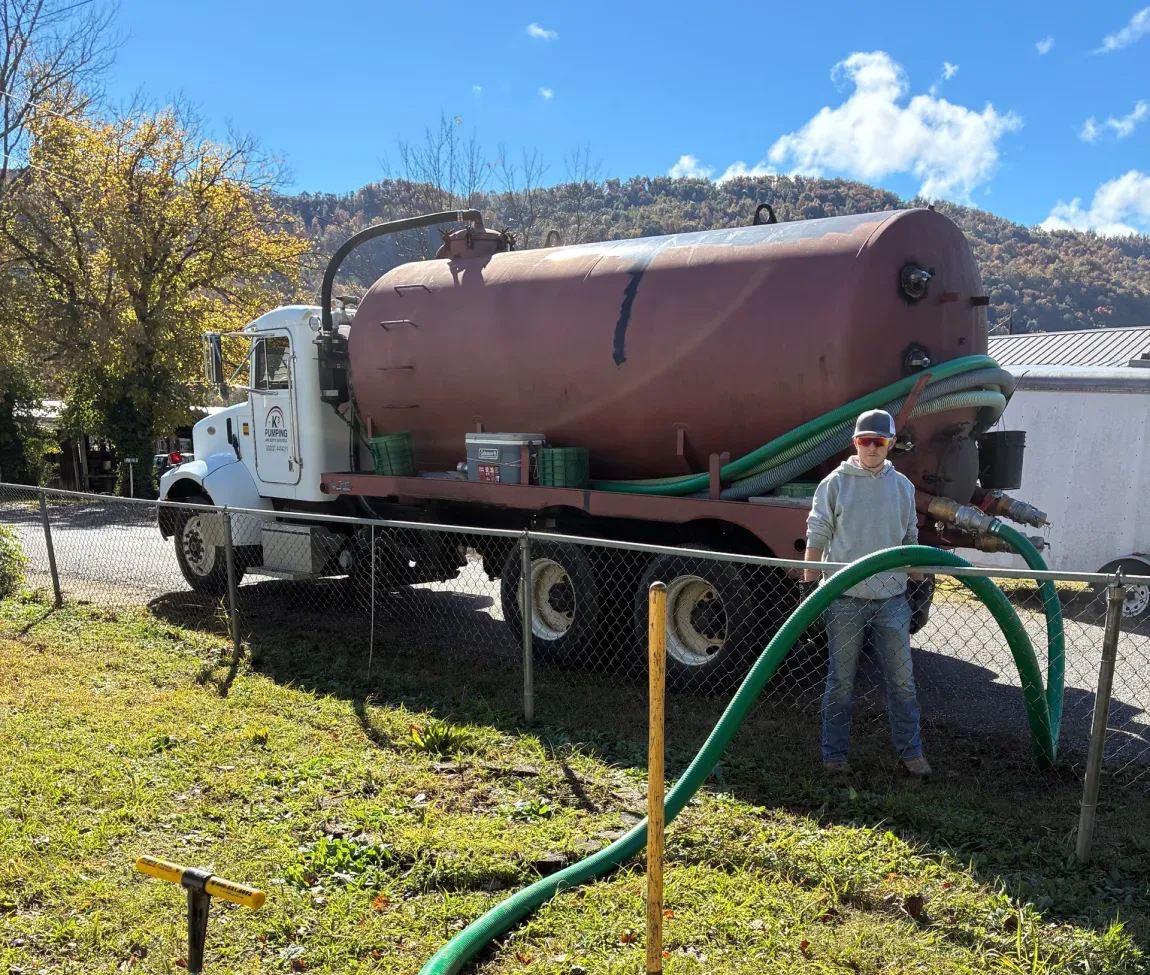 White truck with a large rust-red tank parked outdoors beside a hose, with a person standing nearby