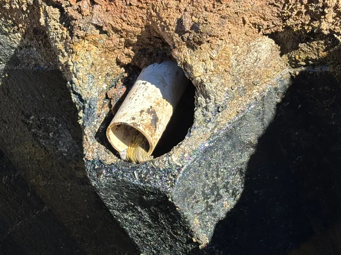 Rusty pipe protruding from a rock or concrete hole in a dark, rough surface