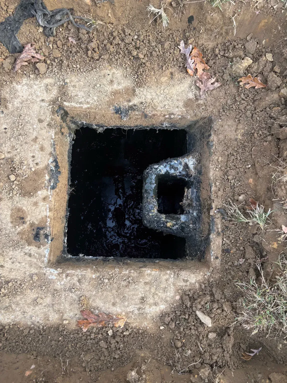 Square concrete pit with a dark opening and a smaller inner opening in the dirt ground.