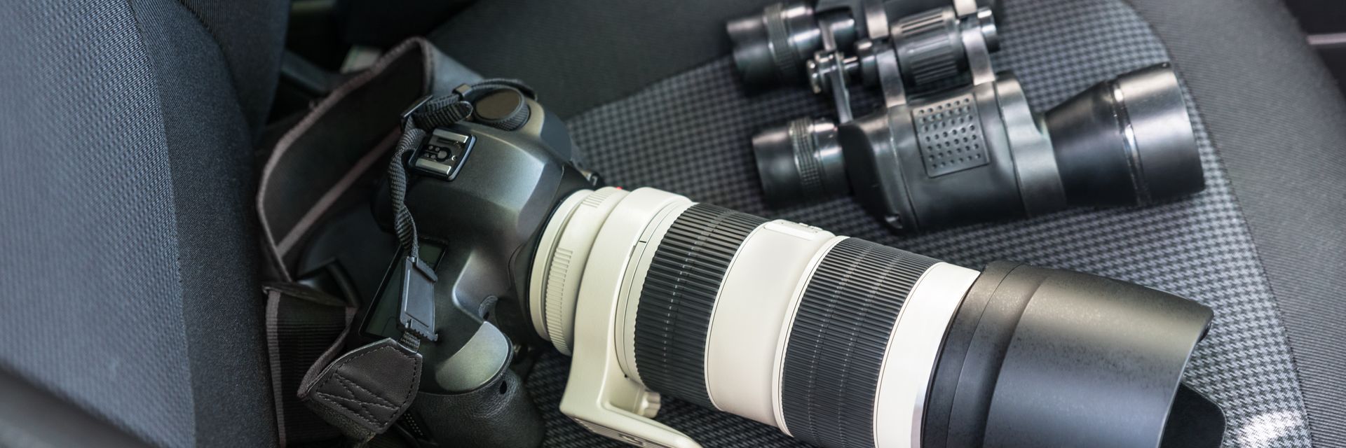 Camera with long white-and-black telephoto lens and other lenses in a padded bag
