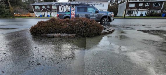 Truck parked near a small, wet garden in front of apartments.