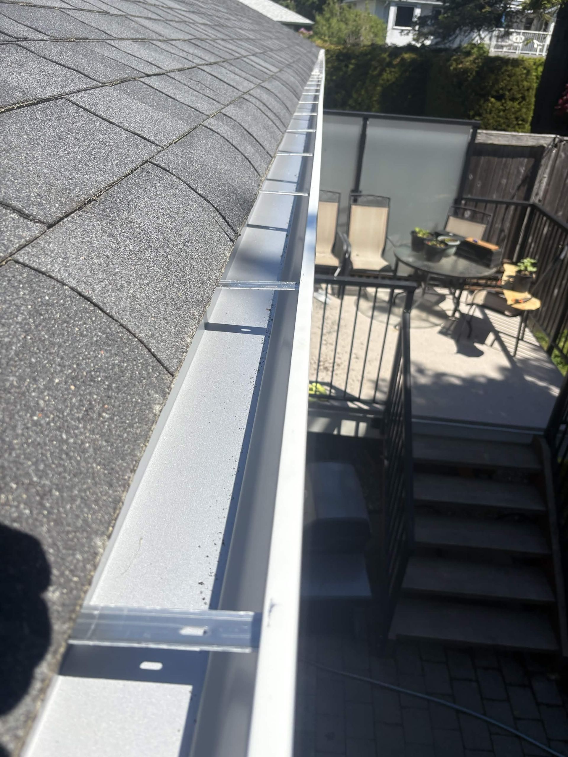 Roof gutter along a gray shingle roof beside a patio with stairs and outdoor furniture