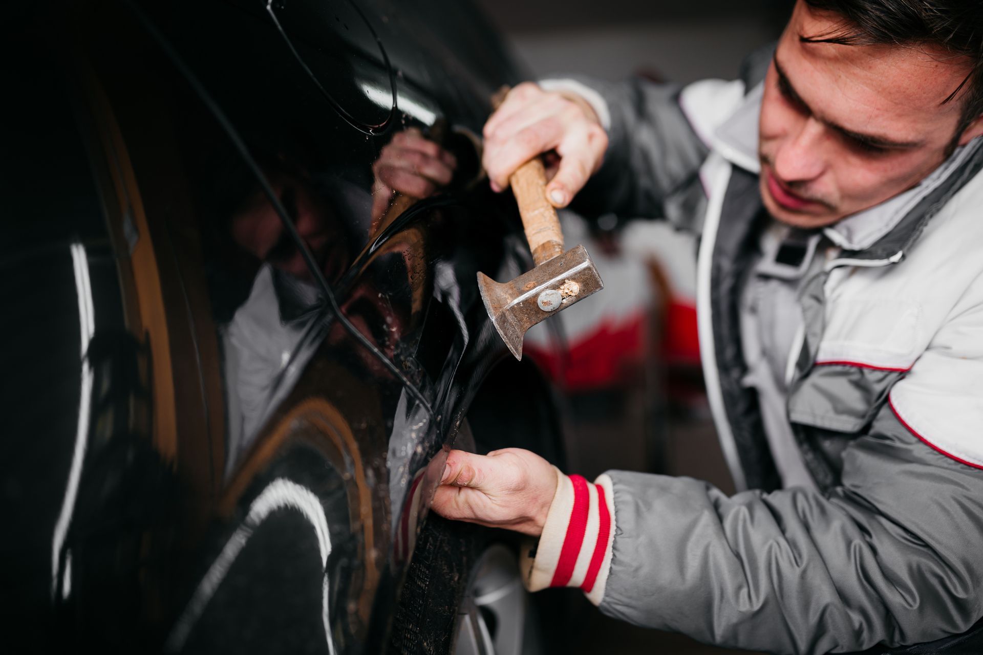 A man is hitting a car with a hammer.