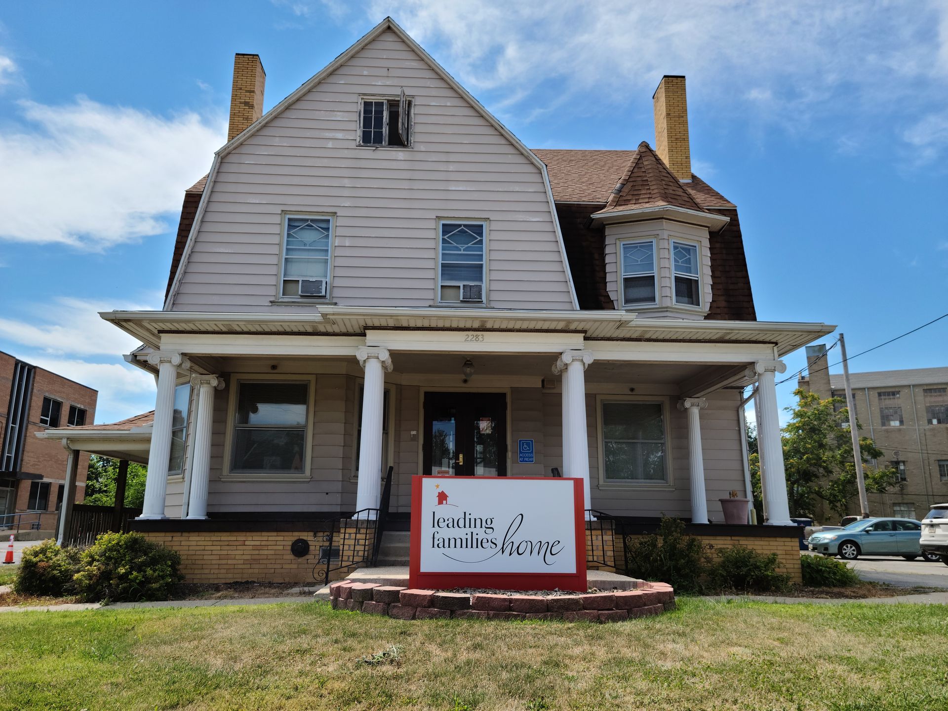 A two-story beige house with a porch; a sign in front says